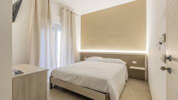 Un dormitorio con cama, mesitas de noche, escritorio, ventana con cortinas y una lámpara de pared.