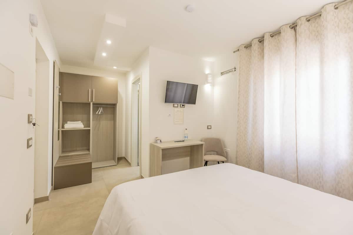 A hotel room with a bed, a desk, a chair, a TV, and a walk-in closet.