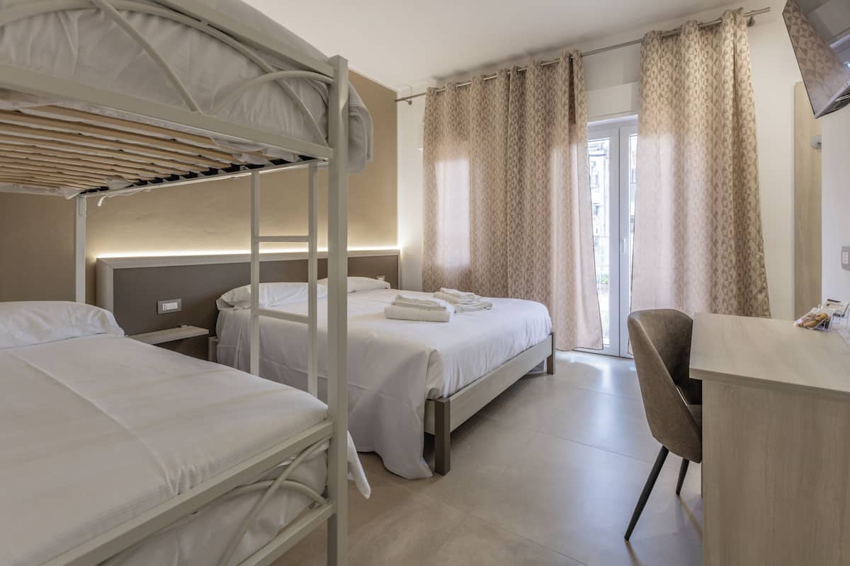 A hotel room with bunk beds, a desk, and a view of the outside.