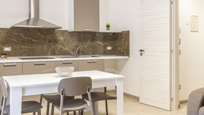 Une cuisine moderne avec un dosseret en marbre, une hotte de cuisine en acier inoxydable et une table à manger blanche avec des chaises.