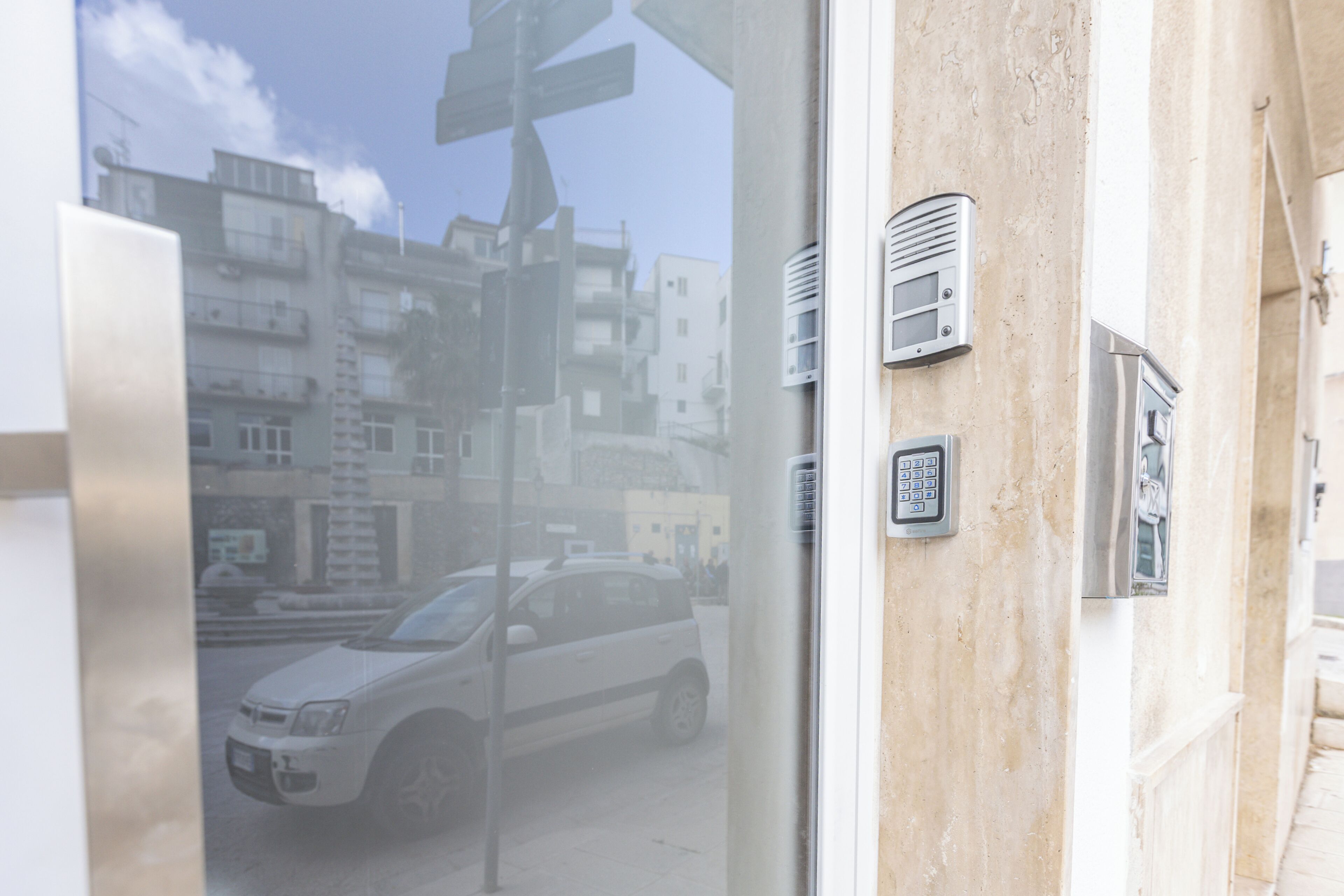 Un edificio con vista a la calle a través de una ventana, que incluye un coche blanco y edificios en el fondo.