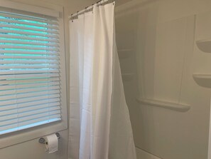 Un bagno con tenda da doccia, porta carta igienica e una finestra con persiane.