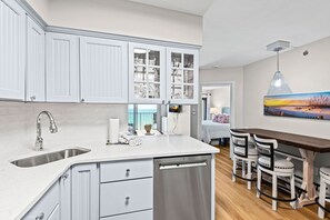 A modern kitchen with white cabinetry, a built-in dishwasher, and a dining area with a wooden table and chairs.