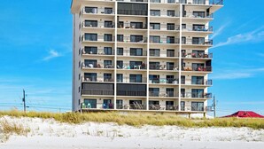 Un hôtel à plusieurs étages doté de balcons, offrant une vue sur la plage et s’ouvrant sur une plage de sable.