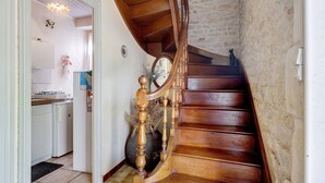 Una escalera de madera con un muro de piedra, una cocina con electrodomésticos blancos y un jarrón decorativo.
