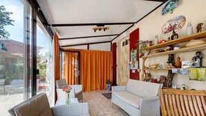 Una habitación iluminada por el sol con muebles de mimbre, una silla de madera y estantes con objetos decorativos.