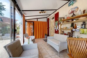 A sunlit room with wicker furniture, a wooden chair, and shelves with decorative items. - Bed and Breakfast 'Chambres D'hôtes Le Peux - Bécacine' with Wi-Fi (Saint-Pierre-le-Vieux)