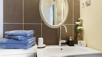Un bagno con lavandino, specchio, pile di asciugamani e articoli da toilette.
