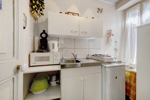 Eine Küche mit weißen Schränken, einer Kaffeemaschine, einem Wasserkocher und einem Kühlschrank.