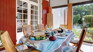A dining area with a table set for four, surrounded by wooden chairs, a patterned tablecloth, and various dishes and condiments.