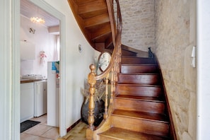 Un escalier en bois avec un mur en pierre, une cuisine avec des appareils électroménagers blancs et un vase décoratif.