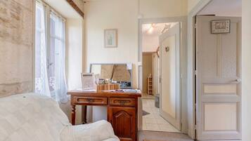 Een kamer met een houten bureau, een witte bank, een lijst met een afbeelding aan de muur, en een deur die naar een andere kamer leidt.