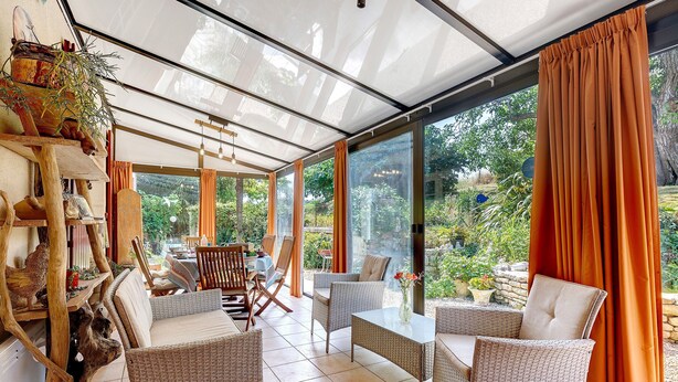 A sunroom with wicker furniture, a dining table, and a view of the garden.