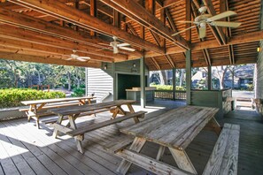 Eine Holzterrasse im Freien mit Picknicktischen und Deckenventilator.