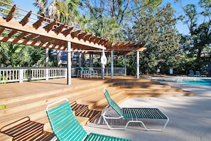 Eine Holzterrasse mit Liegestühlen, einem Pool und einem überdachten Bereich mit Geländer.