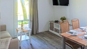 Una habitación con una mesa de comedor, sillas, un televisor montado en la pared y una ventana con cortinas.