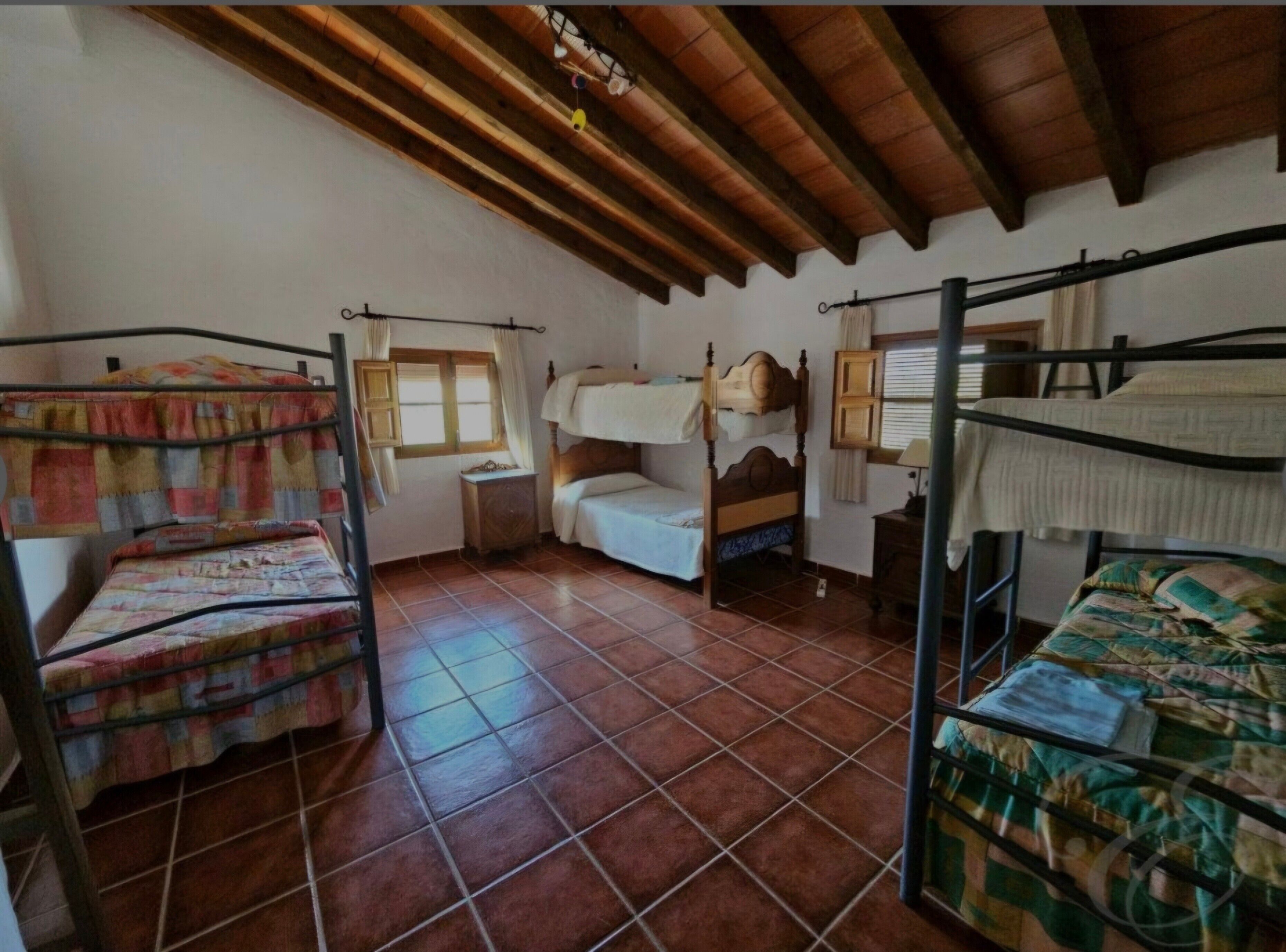 A room with two bunk beds, a wooden ceiling, a window with curtains, and a tiled floor.