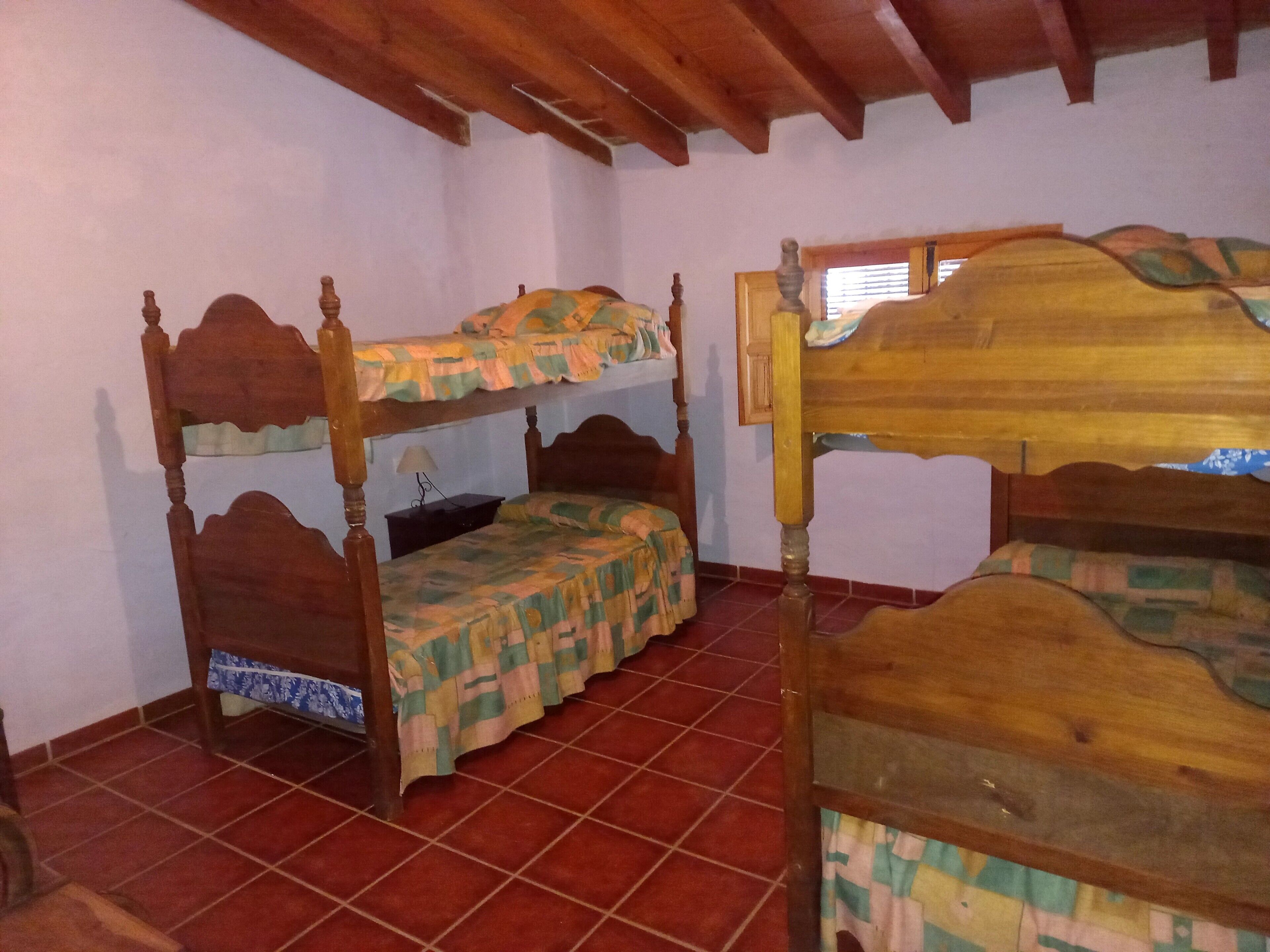Una stanza con due letti a castello in legno, un tavolino con una lampada e un pavimento piastrellato.
