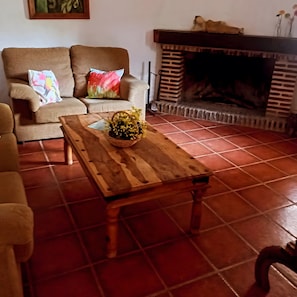 Un saló amb un sofà, una taula de centre de fusta i un arranjament floral, i una llar de foc.