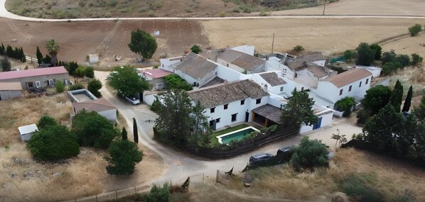 An aerial view of a residential area with houses, a swimming pool, and a road. - Rural House 'La Saucedilla' with Mountain Views, Private Pool and Wi-Fi (Archidona)