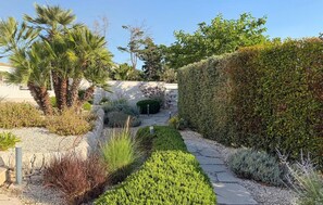 A garden pathway with a stone archway, surrounded by various shrubs and a tall hedge. - Cozy apartment in Reitani with swimming pool (Reitani)