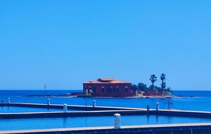 A coastal building with a red roof, adjacent to a clear blue sea. - Cozy apartment in Reitani with swimming pool (Reitani)