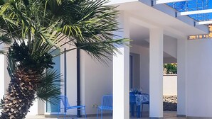 Een overdekt terras met een palmboom, blauwe stoelen en een tafel.