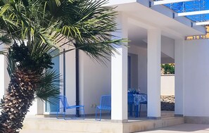 A covered outdoor seating area with a palm tree, blue chairs, and a table. - Cozy apartment in Reitani with swimming pool (Reitani)