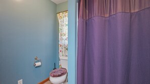 Une salle de bain équipée de toilettes, d’un rouleau de papier toilette, d’un rideau de douche et d’une fenêtre ornée d’un motif coloré.