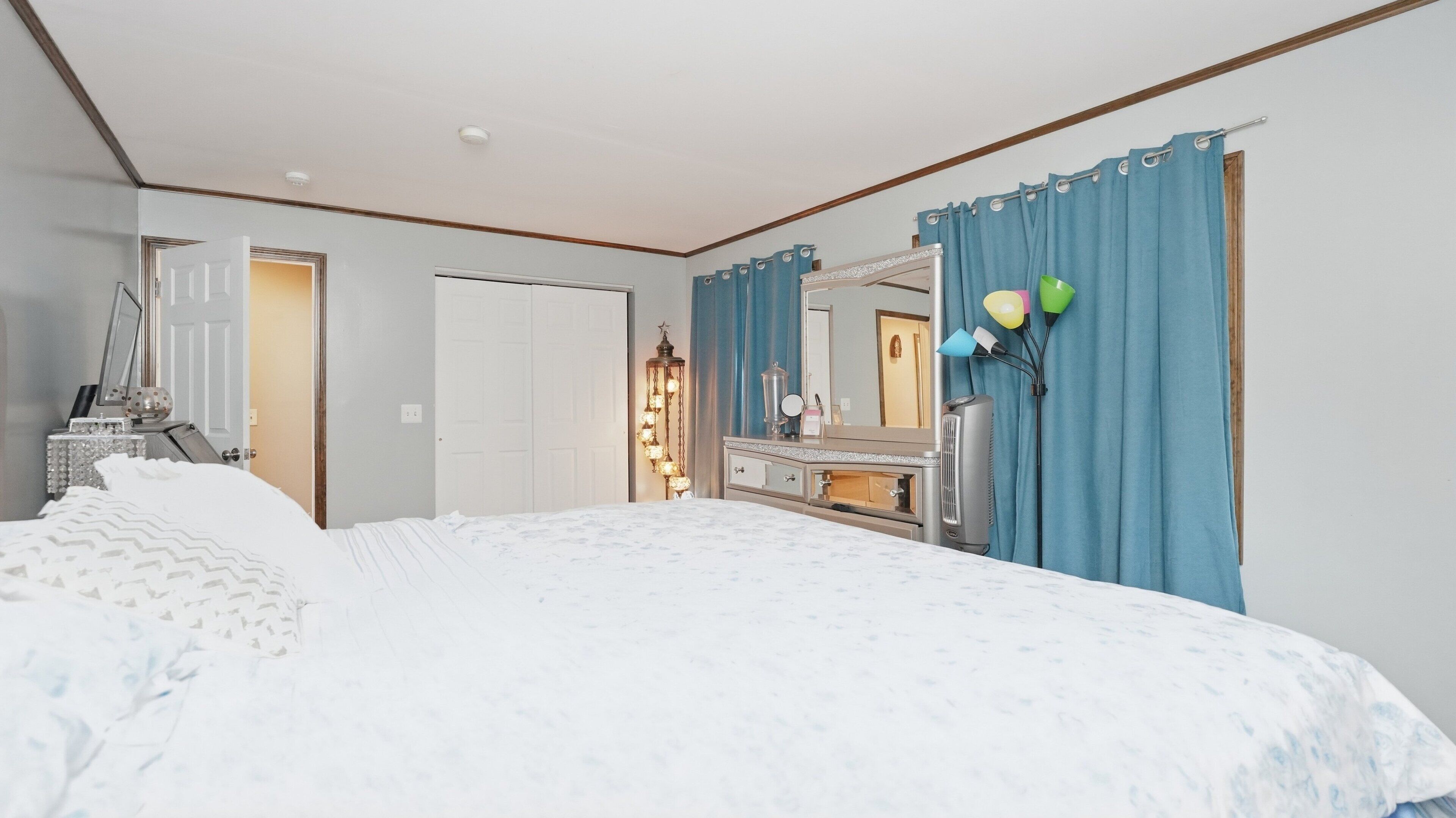 A bedroom with a bed, dresser, vanity, and a mirror.