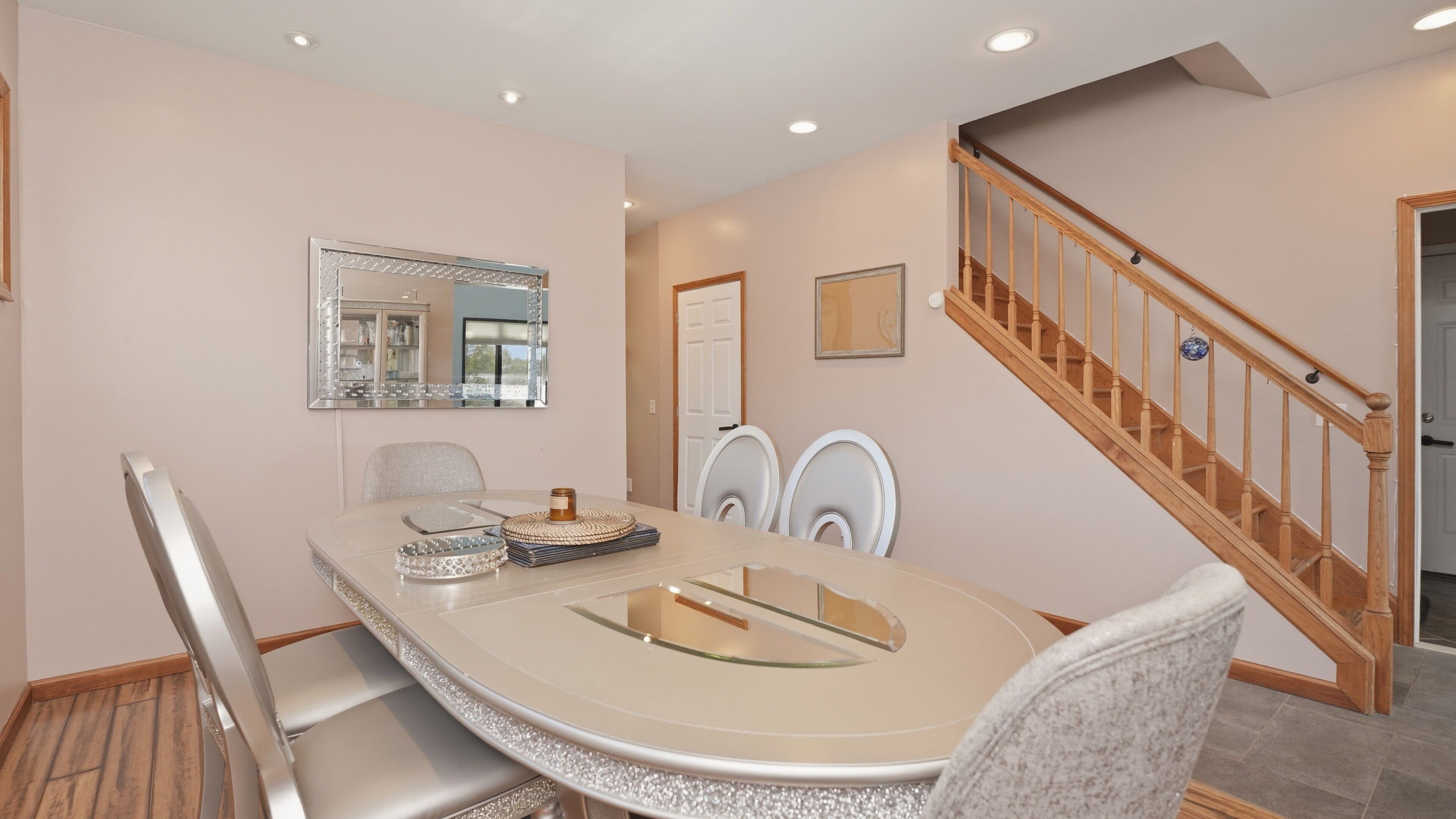 A dining area with a round table, chairs, a mirror, and a staircase.