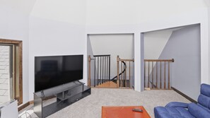 A living room with a flat-screen TV, a staircase, and a blue sofa.