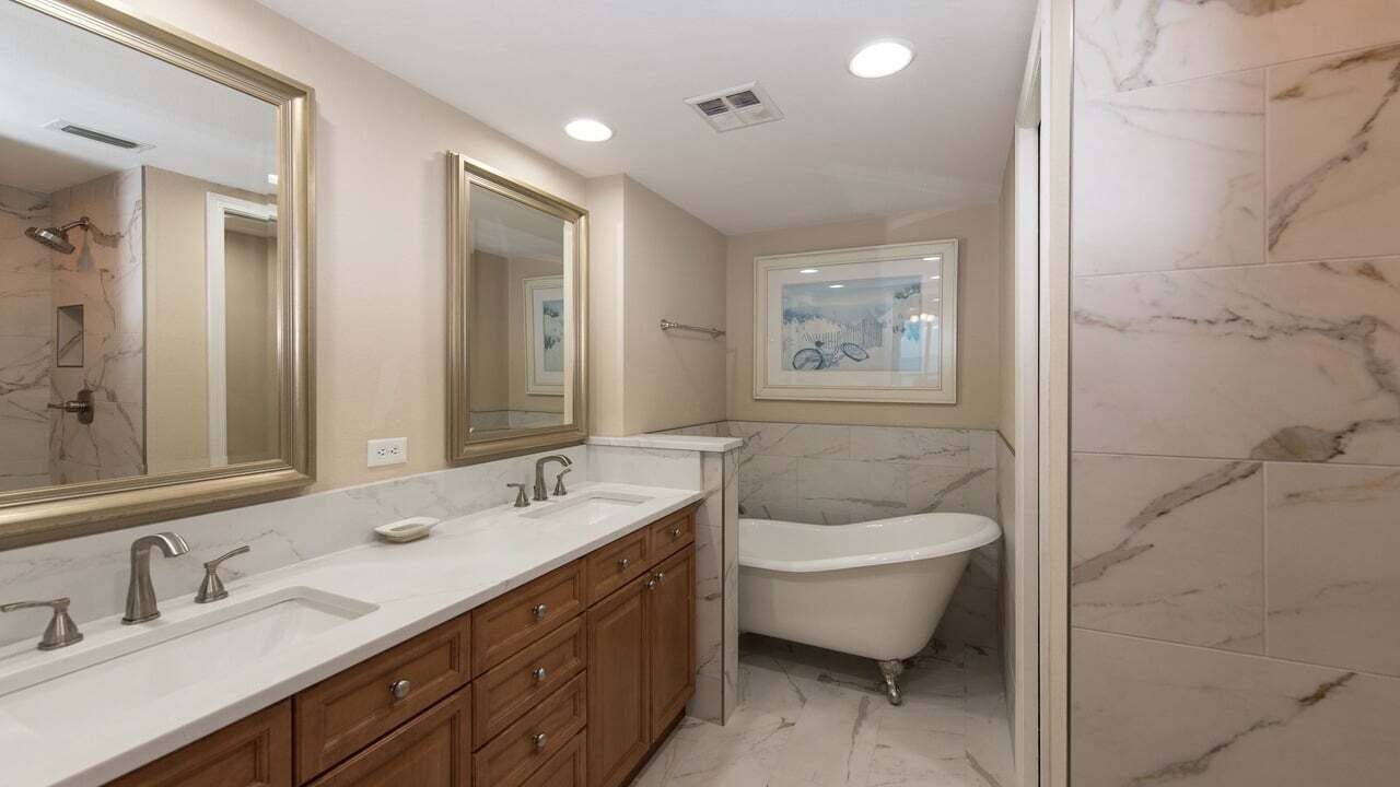 A bathroom with a double sink vanity, a bathtub, and a large mirror.