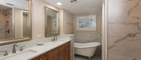 A bathroom with a double sink vanity, a bathtub, and a large mirror.