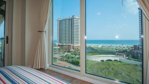 Habitación de hotel con un amplio ventanal que ofrece vistas a un edificio alto y a la playa.