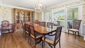 A dining room with a wooden table, chairs, a chandelier, and a cabinet with glass doors. - Beaufort's Pink Paradise, Spacious home, steps away from Front Street (Beaufort)