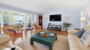 A living room with a sofa, armchair, coffee table, television, and a bookshelf. - Beaufort's Pink Paradise, Spacious home, steps away from Front Street (Beaufort)