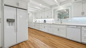 A modern kitchen with white cabinetry, a built-in dishwasher, and a wooden floor. - Beaufort's Pink Paradise, Spacious home, steps away from Front Street (Beaufort)