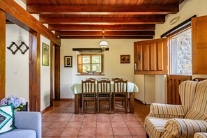 A dining area with a wooden table and chairs, a hanging light fixture, and a stone wall.