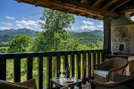 A wooden balcony with wicker furniture, a table with a bottle and glasses, and a scenic mountain view.. Casa la Xerra with Spectacular Views