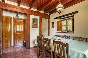 A dining area with wooden chairs, a table with a tablecloth, a hanging light fixture, and a window with a view.