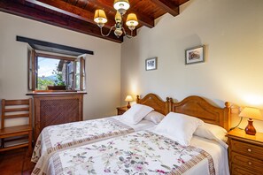 A bedroom with a wooden headboard, two bedside tables with lamps, a window with a view, and a wooden chair.
