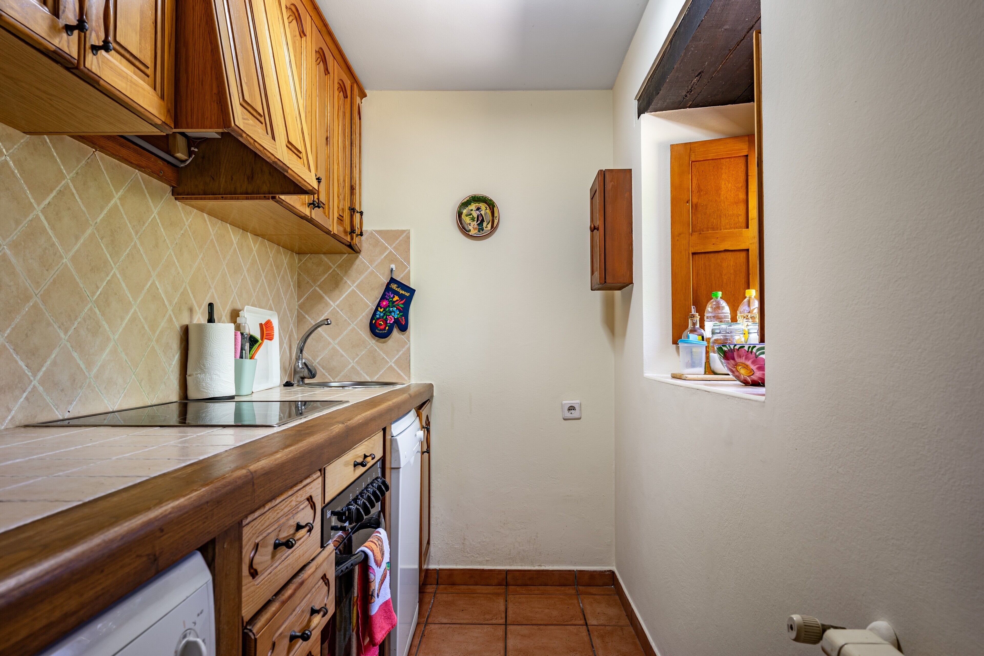 Cocina con armarios de madera, salpicadero de azulejos, ventana con vistas y un plato colgado en la pared.