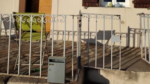 A building with a wooden door, a window with shutters, a metal fence, and a green chair. - Large, comfortable house with terrace overlooking the valley. (Sant'Andréa-di-Bozio)