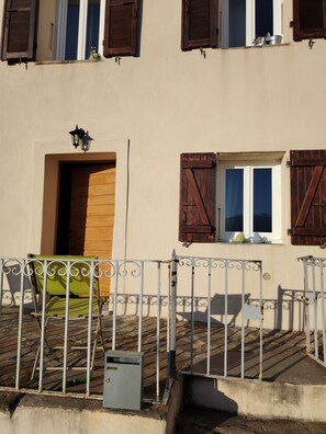 A building with a wooden door, a window with shutters, a metal fence, and a green chair. - Large, comfortable house with terrace overlooking the valley. (Sant'Andréa-di-Bozio)