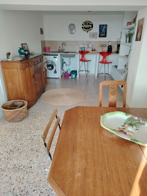 A kitchen with a washing machine, a sink, and a dining area with a table and chairs. - Large, comfortable house with terrace overlooking the valley. (Sant'Andréa-di-Bozio)