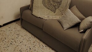 A living room with a sofa, a lamp, a wall-mounted sun decoration, and a framed picture. - Large, comfortable house with terrace overlooking the valley. (Sant'Andréa-di-Bozio)