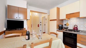 A compact kitchen with wooden cabinets, a built-in oven, and a dining area with a checkered tablecloth.