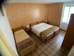 Un dormitorio con dos camas, paredes de madera, una ventana y una mesita de noche con lámpara.