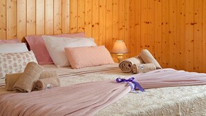 A neatly made bed with pink linens, a rolled towel, and a purple ribbon.